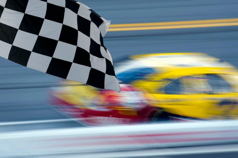 Race car blurred on track against rail with checkered flag