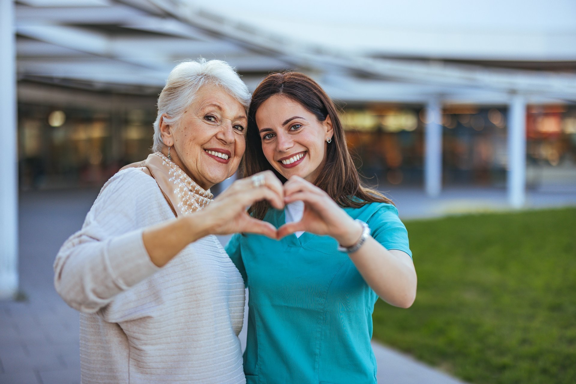 Elderly woman and caregiver forming heart shape outdoors
