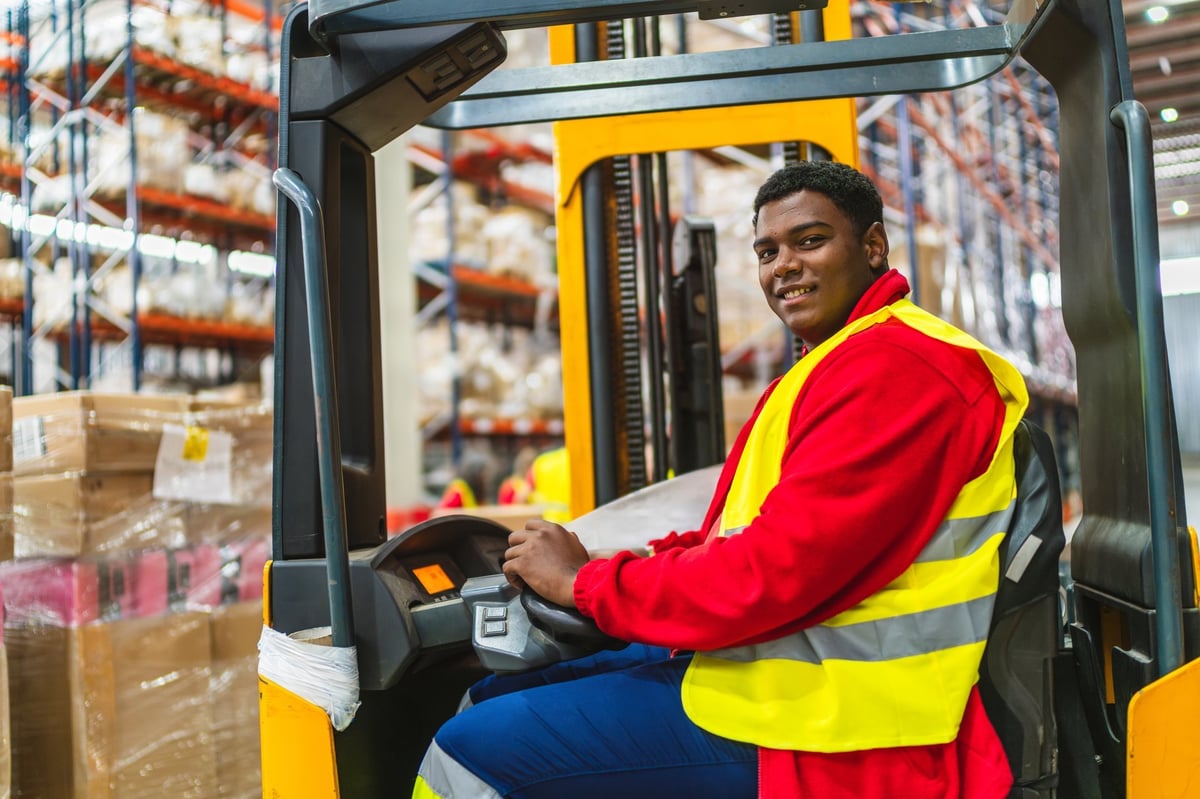 Young warehouse worker drives a forklift, organizing goods on shelves, ensuring smooth logistics. Professional and dedicated, they manage the warehouse efficiently