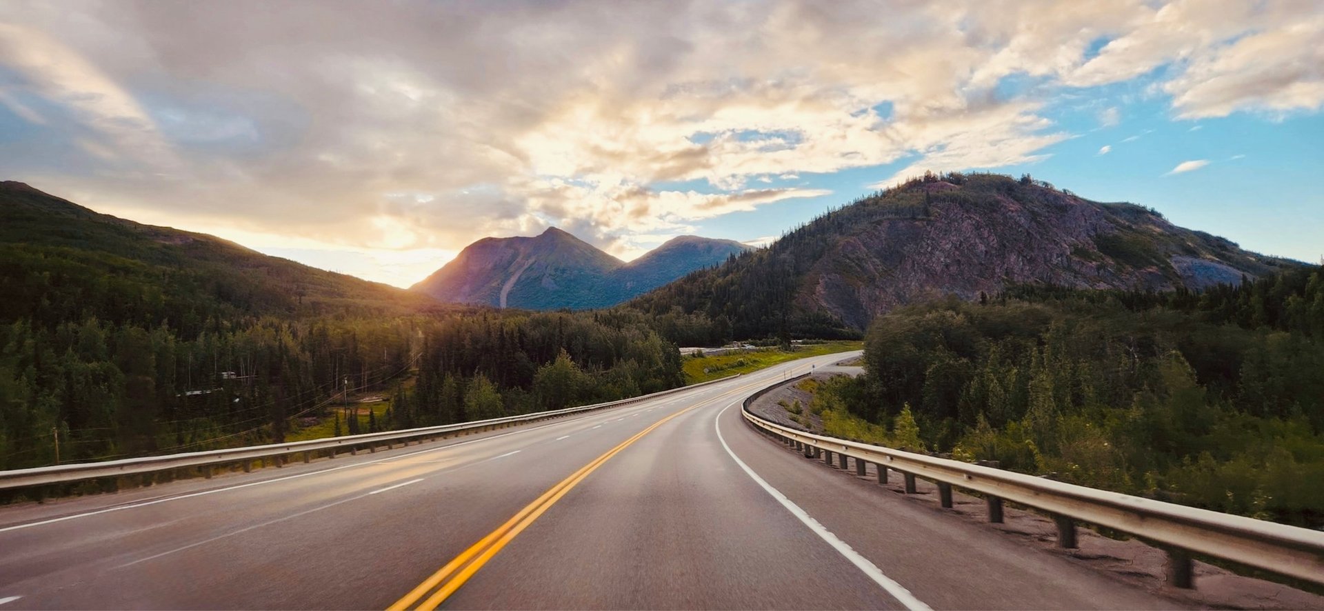 Scenic road going through large Alaskan mountains in sunset time