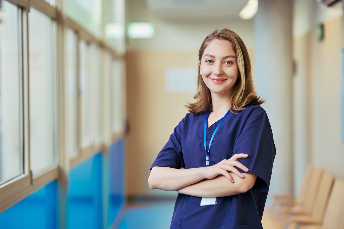 Portrait of a young nurse smiling with crossed arms, showcasing confidence and professionalism in a modern hospital environment