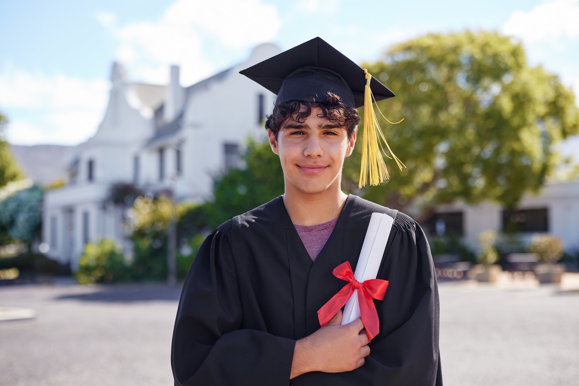 Smiling graduate male student holding degree wearing cap and gown, proud academic celebration achievement