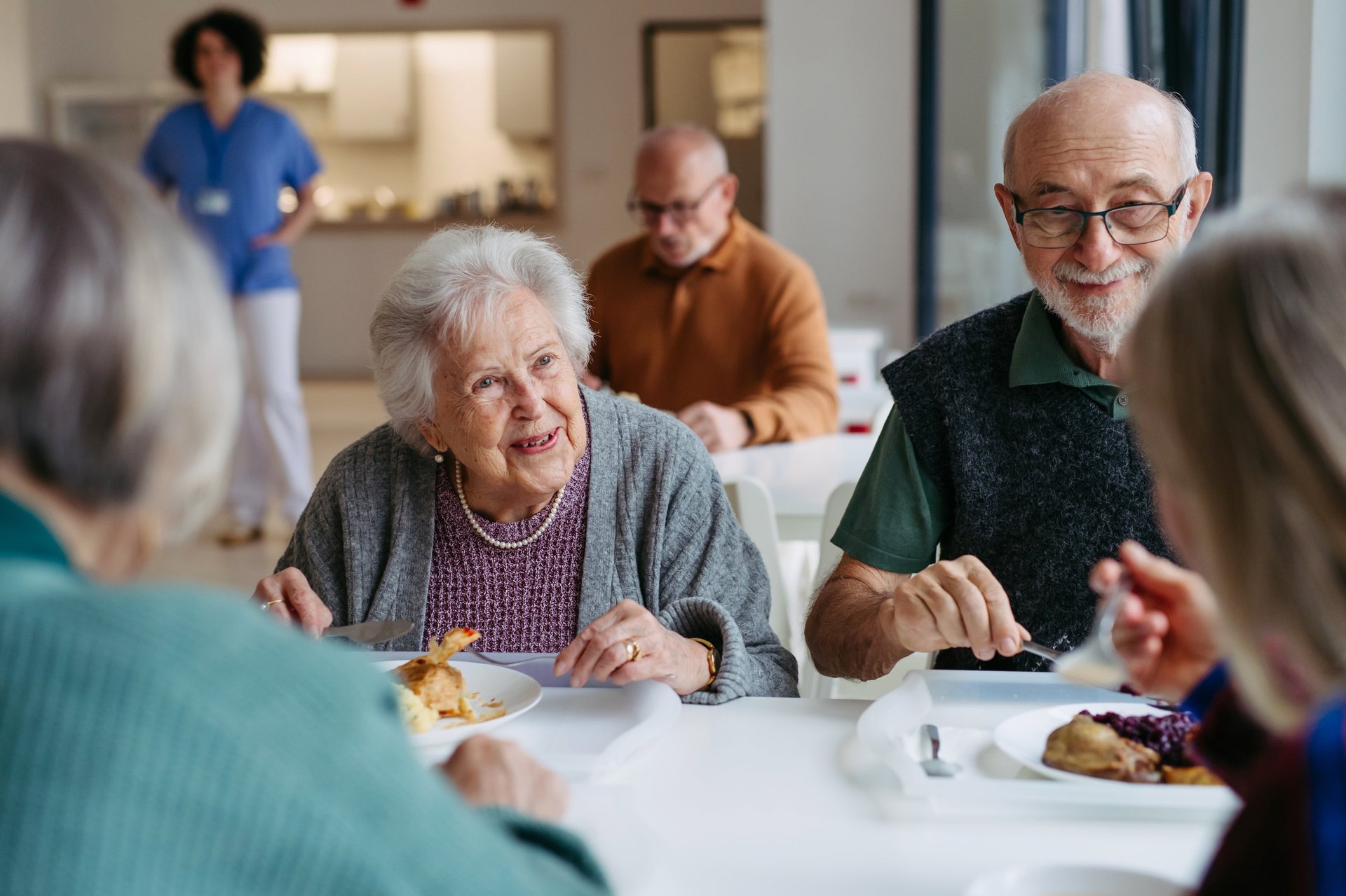 Group of elderly people having lunch with supportive caregiver in community center cafeteria
