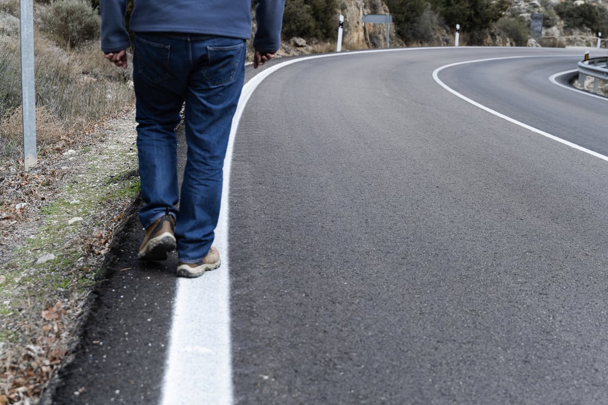 Person walking on a road curve with limited visibility, increasing accident risk.