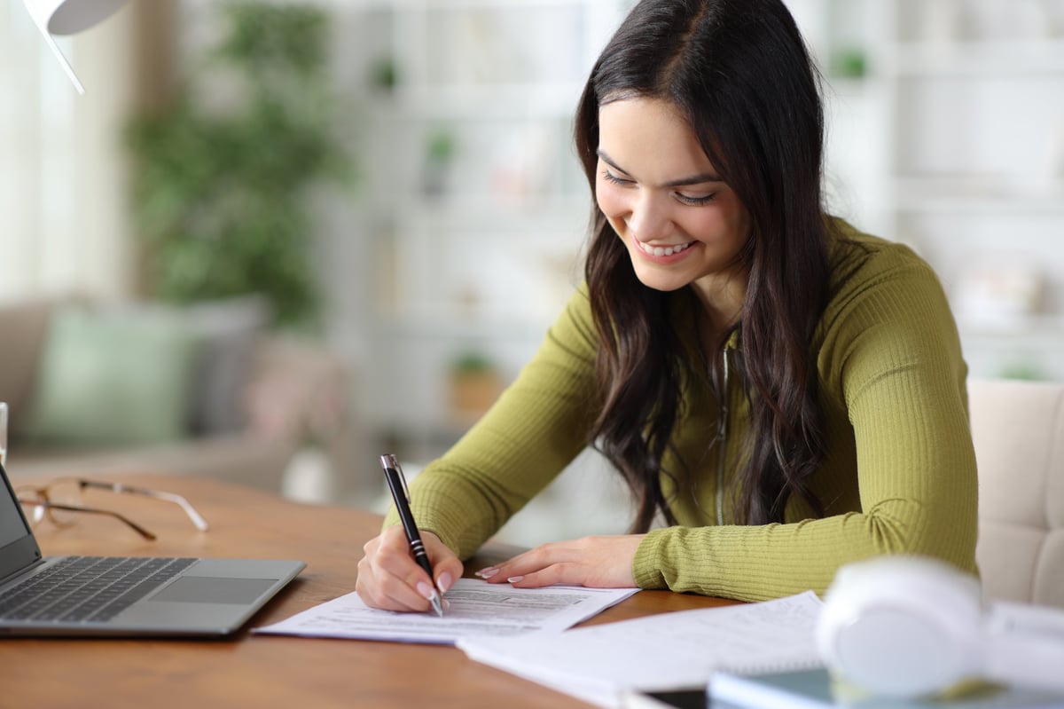 Happy young student filling out a paper application form on a wooden table at home
