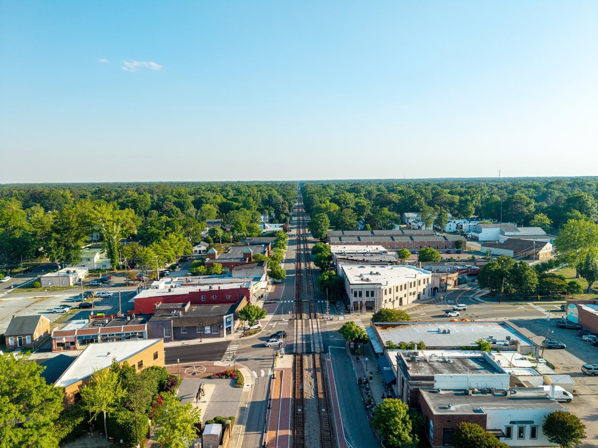 Ashland, Virginia, aerial view looking straight down the historic train tracks running through the center of the downtown district lined with small businesses, trees, and roads.
