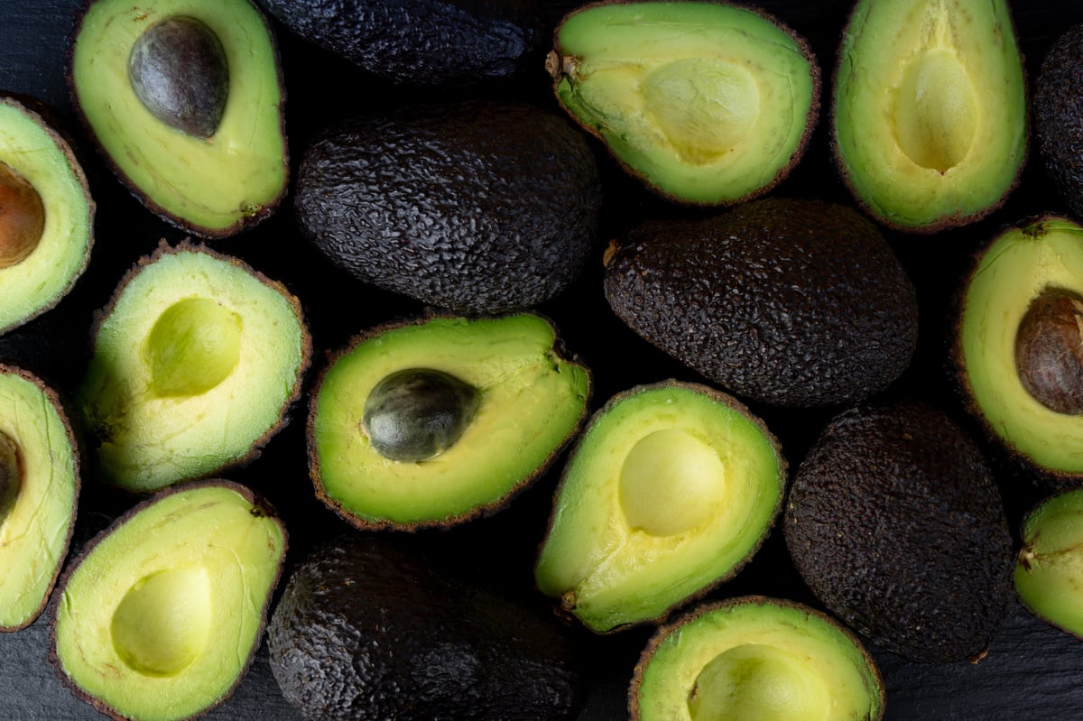Many Hass Avocado Halves on Black, Whole Sharwil, Brown Avocados Cut, Fresh Alligator Pear, Guacamole Ingredient, Persea Americana Avocado Fruit Top View