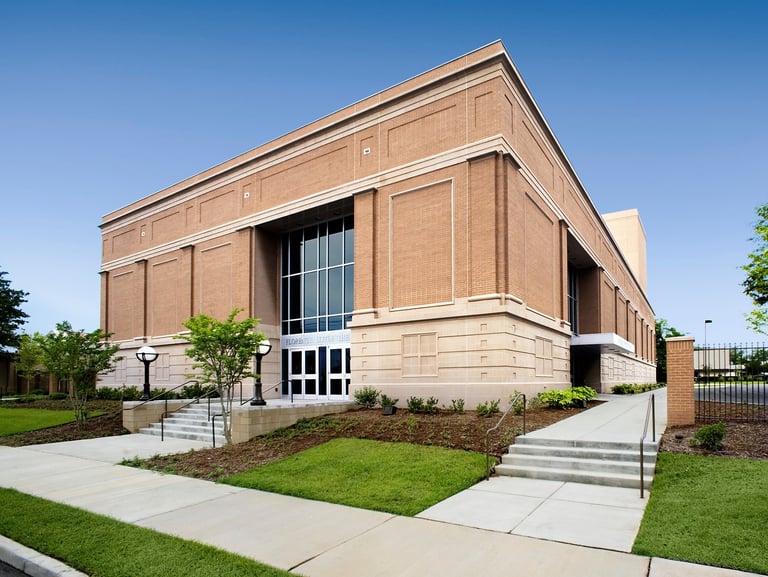 Modern brick building with large windows and entrance steps, surrounded by manicured lawn and landscaping