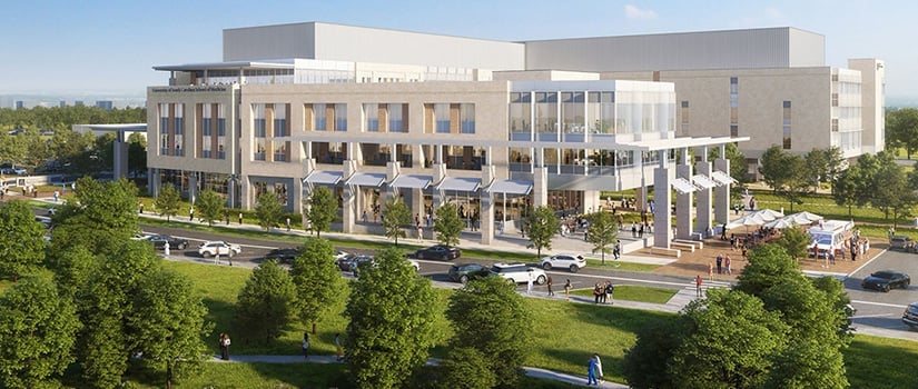 Modern multi-story institutional building with white and tan facade, glass windows, and columned ground level surrounded by green landscaping and parking area