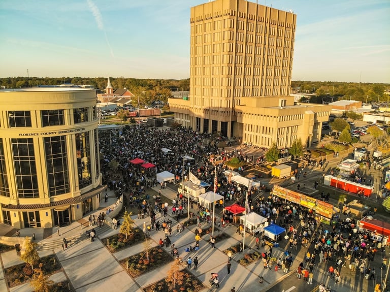 Aerial view of a crowded city plaza with large brick buildings, food trucks, and festival tents during daytime