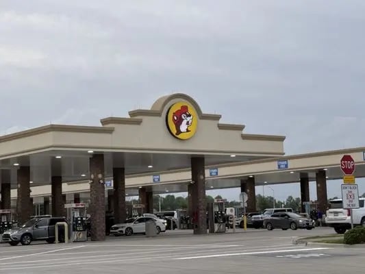 Buc-ees gas station and convenience store exterior with iconic mascot logo on roof and canopy with parked vehicles